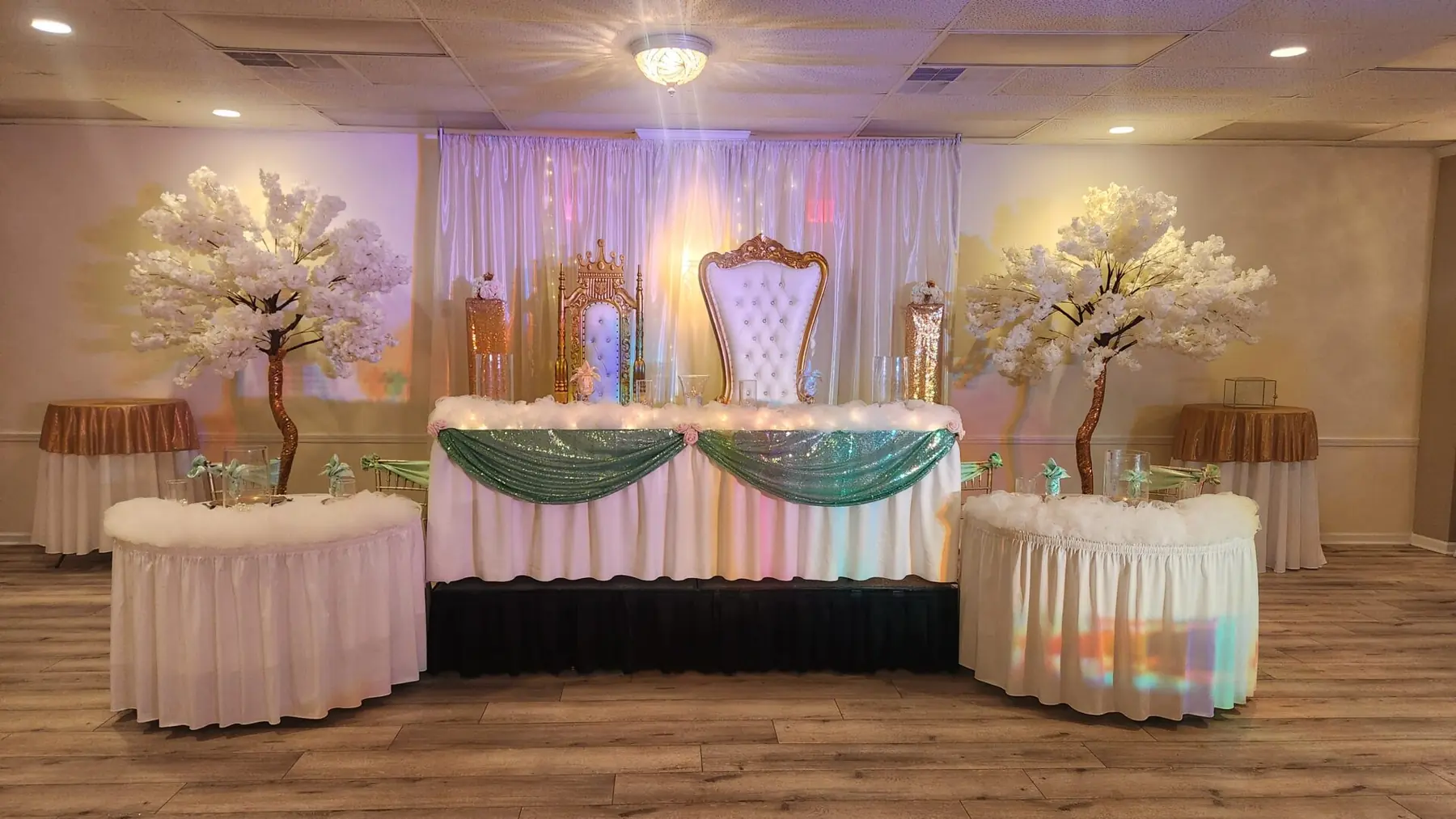 A head table with a throne chair, sage swags and white blossom trees