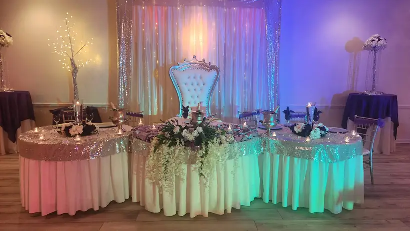 A sweetheart table with a white throne chair and color-washed drapery