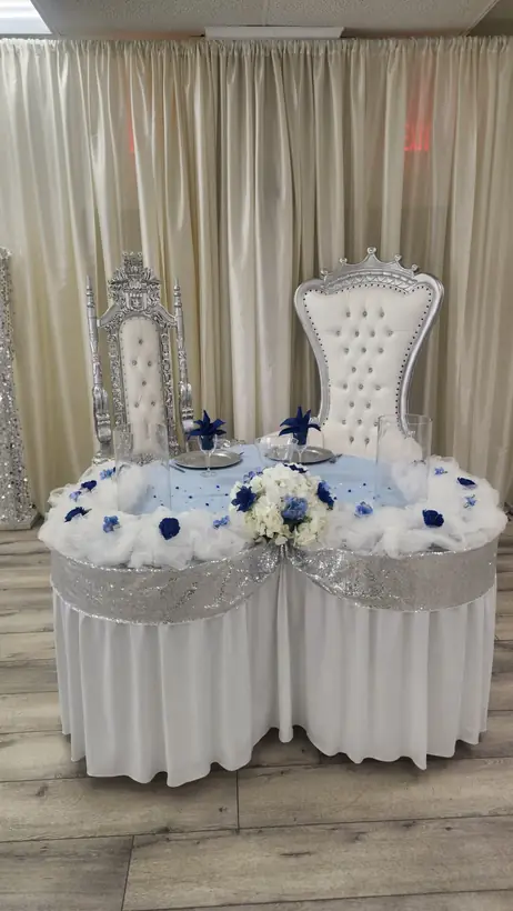 Two silver and white throne chairs behind a table trimmed in white and navy roses