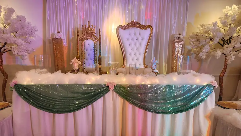 Two throne chairs behind a head table draped in sage sequin swags