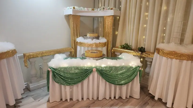 A cake table with gold columns and sage sequin swags