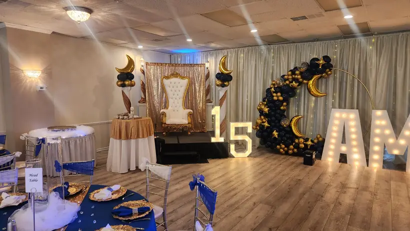 Navy and gold quinceañera tables before a throne and a crescent balloon arch