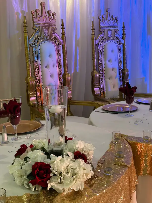A red and white rose centerpiece before two gold throne chairs